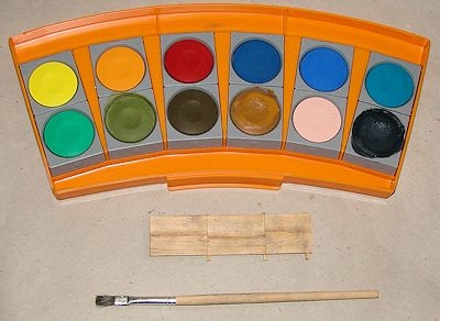 Wasserfarbkasten, Pinsel und der gealterte Bauzaun