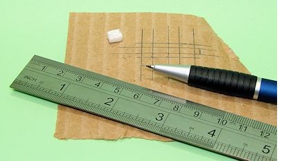 Metalllineal, Druckbleistift, Styroporstückchen liegen auf einem Pappstreifen, der mit Maßzeichnungen versehen ist