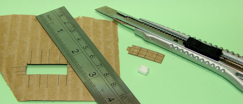 Bastelmesser, Metalllineal, ausgeschnittenes Pappstückchen, Styroporquader